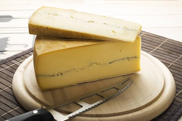 Big piece of cut cheese on a wooden plate with a knife by