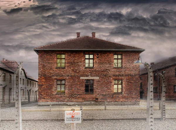 Dom murowany za ogrodzeniem z drutu kolczastego i stół z ostrzeżeniem w języku niemieckim. Więzienie z czasów II wojny światowej. — Zdjęcie stockowe