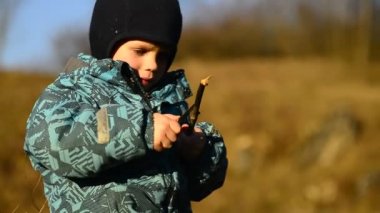 Küçük çocuk tahta bir sopayı bilemek için keskin bir bıçak kullanıyor. Gerçek hayatta gerçek aletle oynanır. Çocuk gerçek alet kullanıyor. Çocuk büyütmek. Sert ışık ve gölgeler.