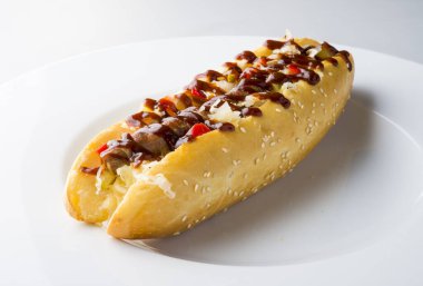 Beyaz tabakta ketçaplı ızgara sosisli sandviç.