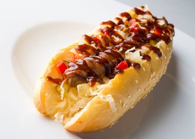 Beyaz tabakta ketçaplı ızgara sosisli sandviç.