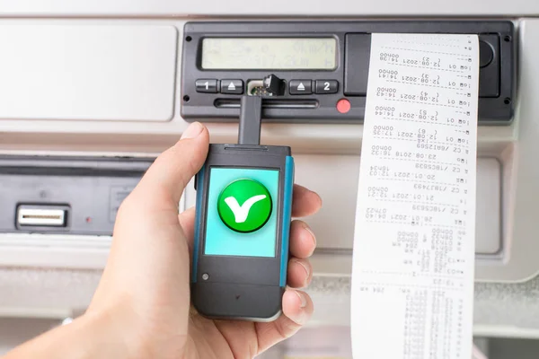 Sürücü elinde yeşil onay işaretli dijital bir tachograph okuyucusu tutuyor. Tachograph indirmesi. Kontrol.