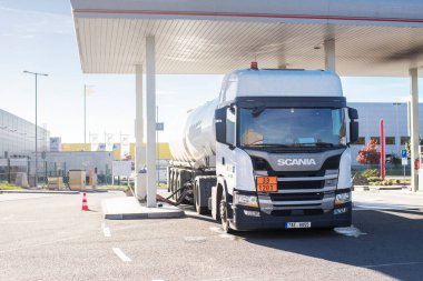 White fuel tanker truck at a petrol station connected by a hose to the underground tanks and refelling it