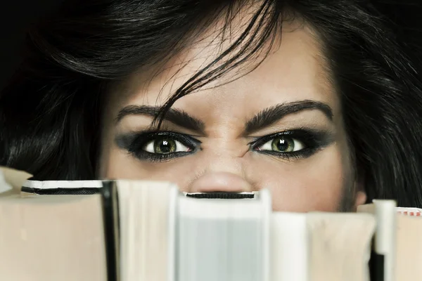 Angry girl hiding behind book shelf — Stock Photo, Image