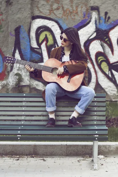 Девушка сидит на скамейке и играет на гитаре — стоковое фото