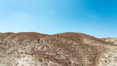 Yürüyüşçüler çöl bölgesinde yüksek bir tepeye tırmanırlar.