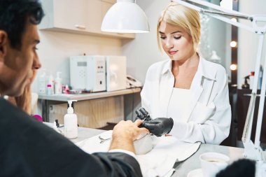 Tırnak törpüsüyle erkek tırnağı üzerinde çalışan kadın tırnak teknisyeni.