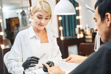 Güzellik uzmanı tırnak cilasından sonra erkek parmağını kontrol ediyor