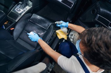 Araba servisi çalışanı otomobilin ön koltuğunu temizliyor.