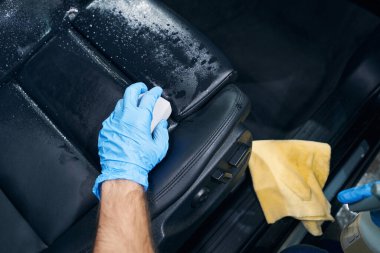 Araba servisi çalışanı deri koltuğu süngerle siliyor.