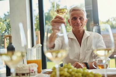 Elinde şarap kadehi tutan gülümseyen bir erkek.
