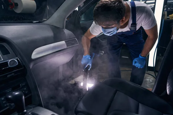 Trabajador en la máscara de seguridad limpieza por soplado salón de automóviles con productos químicos —  Fotos de Stock