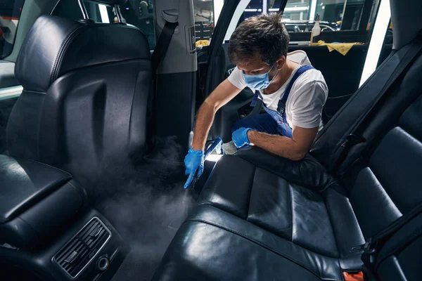 Trabajador que quita la suciedad incorporada del salón del coche con el limpiador de vapor —  Fotos de Stock