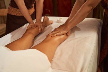 İki Taylandlı masaj uygulayıcısı beyaz müşteri bacak kaslarını esnetiyor.