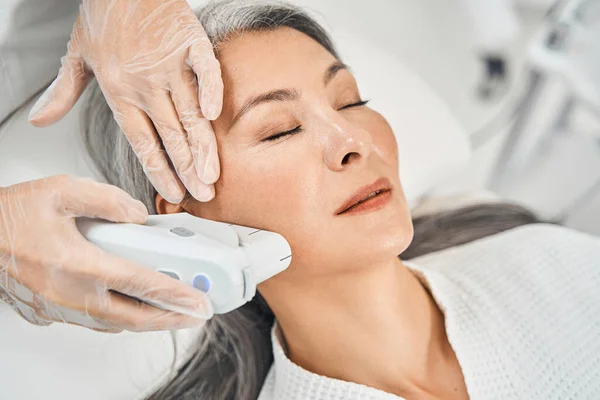 Pleased Asian patient enjoying the procedure of smoothing skin — Stock Photo, Image