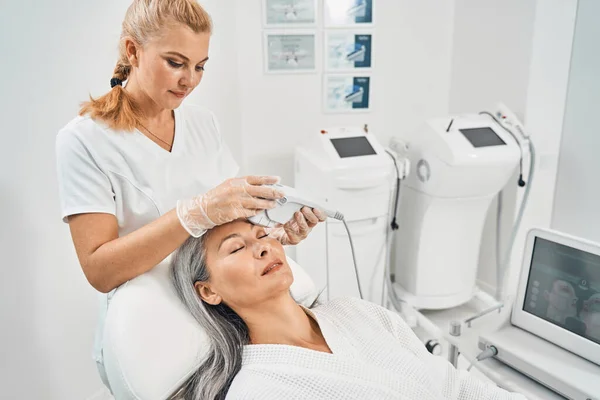 Attentive beautician doing face lifting for patient — Stock Photo, Image