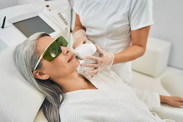 Mujer de pelo gris encantada positiva mirando a su cosmetólogo — Foto de Stock