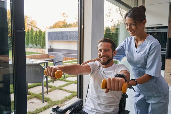 Kobieta pielęgniarka asystentka pomaga mężczyźnie z niepełnosprawnością fizyczną w nowoczesnych apartamentach — Zdjęcie stockowe