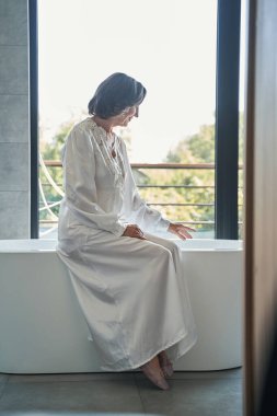 Küvette su ısısını ölçen yaşlı bir kadın.