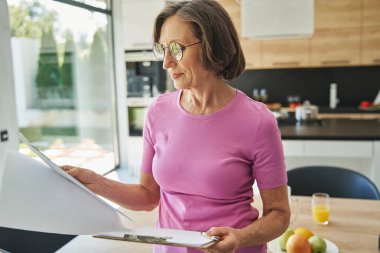 Odaklanmış yaşlı kadın, panodan kağıt okuyor.