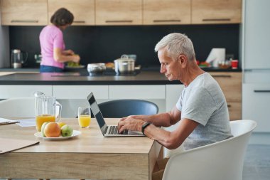 Mutfakta dizüstü bilgisayarda çalışan kıdemli bir adam.