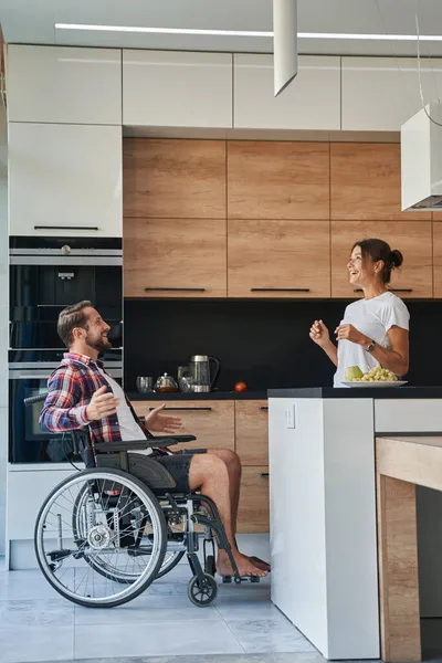 Красивий чоловік, який використовує інвалідне крісло, розмовляє зі своєю красивою дівчиною в їхньому будинку — стокове фото
