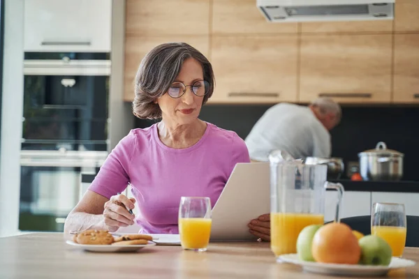 Концентрована літня жінка читає документ під час сніданку — стокове фото