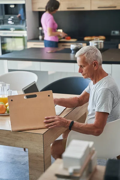 Старший мужчина открывает папку документа во время работы на ноутбуке — стоковое фото