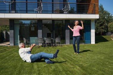 Yaşlı bir adam çimlere uzanıp karısının fotoğrafını çekiyor.