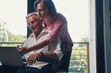 Tekerlekli sandalyeyle dizüstü bilgisayarda bir şeye gülen yaşlı adam.
