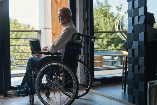 Wesoły człowiek z paraplegią pracujący na laptopie — Zdjęcie stockowe