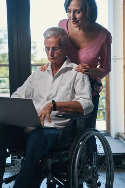 Kobieta patrząc na laptopa użytkownika wózka inwalidzkiego zza ramienia — Zdjęcie stockowe