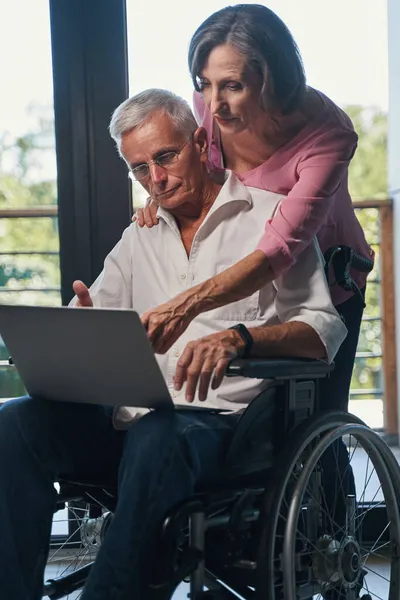 Yaşlanan kadın tekerlekli sandalye kullanıcısının dizüstü bilgisayarını işaret ediyor — Stok fotoğraf