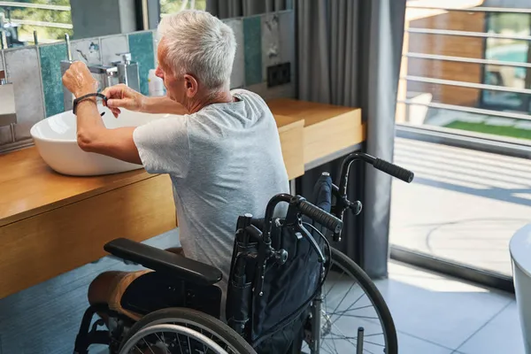 Starsza osoba niepełnosprawna zdejmująca smartwatch podczas mycia rąk — Zdjęcie stockowe