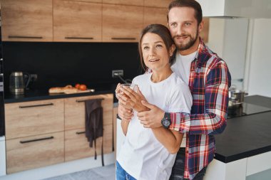 Yakışıklı bir adam, modern apartmanlarda elinde içki bardağıyla kız arkadaşına sarılıyor.