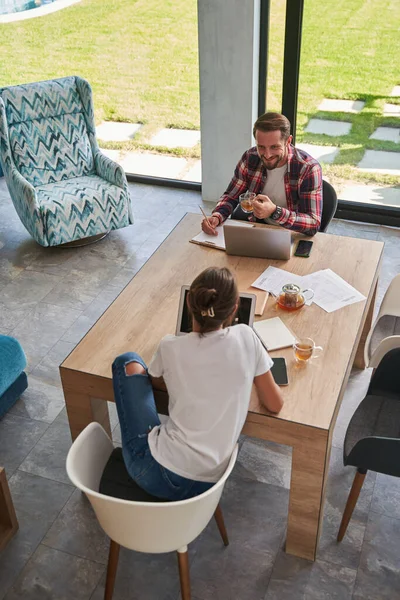 Bonito homem trabalhando online com encantadora fêmea em laptops na xícara de bebida no quarto dentro de casa — Fotografia de Stock