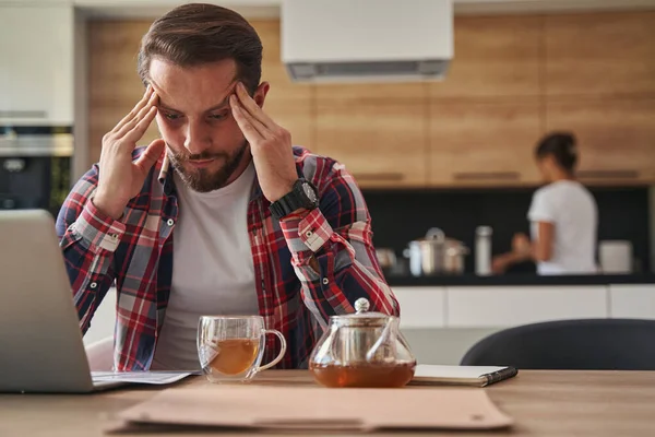 Snygg vit man i skjorta håller huvudet med händerna medan du arbetar på laptop från hemmakontoret — Stockfoto