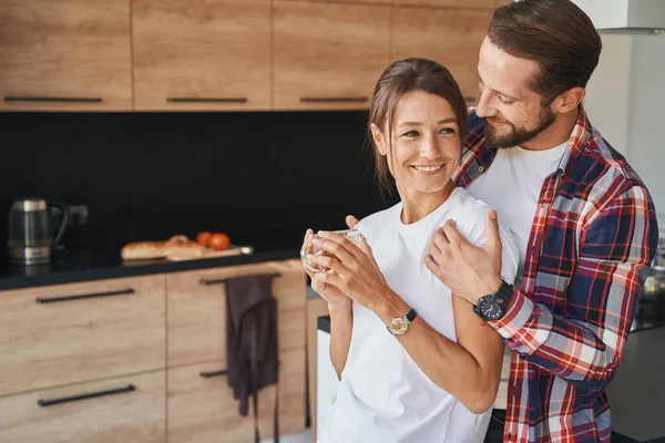 Yakışıklı sakallı erkek modern mutfakta kız arkadaşına sarılıyor. — Stok fotoğraf