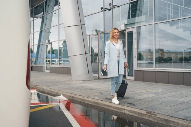 Havaalanı terminali yakınlarında bagajı olan mutlu bir turist.