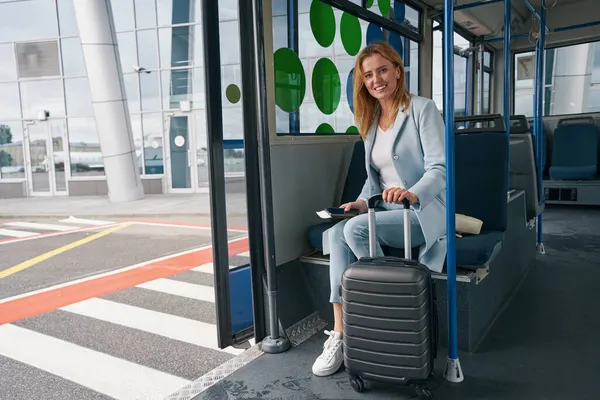 Stilvolle Dame mit Gepäck sitzt im geparkten Flughafen-Shuttlebus — Stockfoto