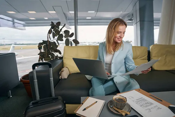 Aangename zakenvrouw die documenten doorneemt in de luchthavenlounge — Stockfoto