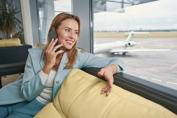 Vrolijke toerist in gesprek op smartphone in de lounge van de luchthaven — Stockfoto