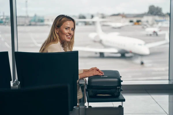 Cheerful traveler with luggage sitting in airport lounge — Stock Photo, Image