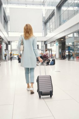 Havaalanı terminali boyunca bavul taşıyan kadın yolcu.