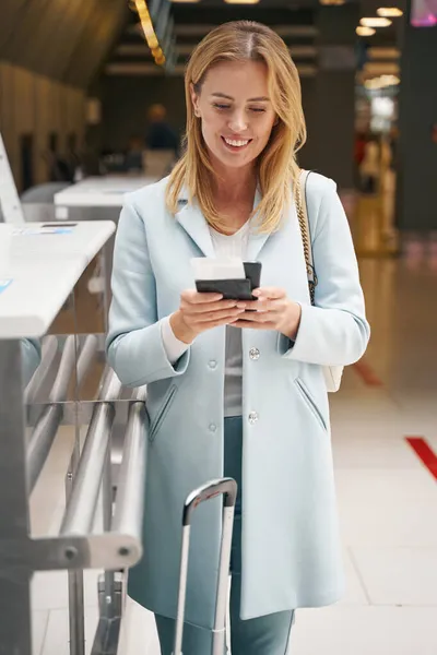 Vreugdevolle passagier met haar smartphone op luchthaventerminal — Stockfoto