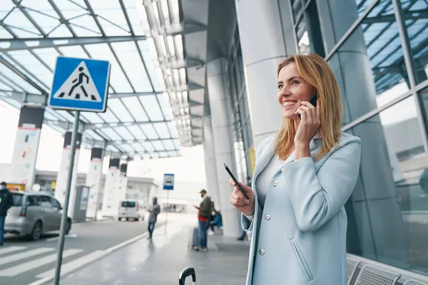 Vreugdevolle vliegtuigreiziger die een telefoongesprek heeft in de buurt van luchthavengebouw — Stockfoto