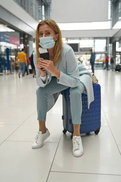 Малодушний турист в масці для обличчя сидить на її багажі — стокове фото