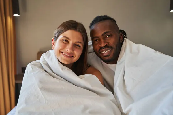 快乐的男女混血夫妻坐在床上 — 图库照片