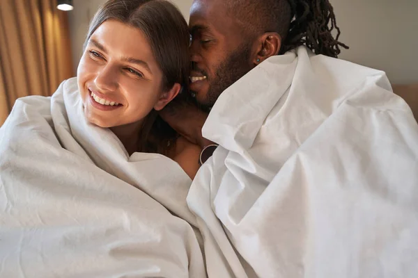 一对浪漫的混血夫妇裹着羽绒被坐在床上 — 图库照片