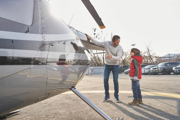 Веселий маленький хлопчик слухає тата біля гелікоптера. — стокове фото